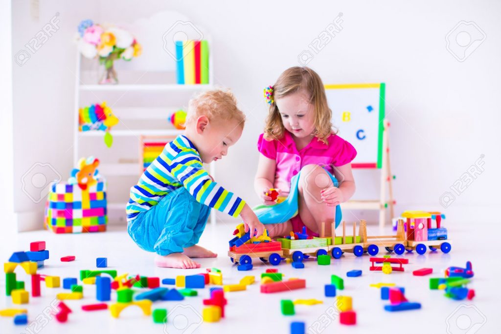 Kids play at day care. Two toddler children build tower of colorful wooden blocks. Child playing with toy train. Educational toys for preschool and kindergarten.